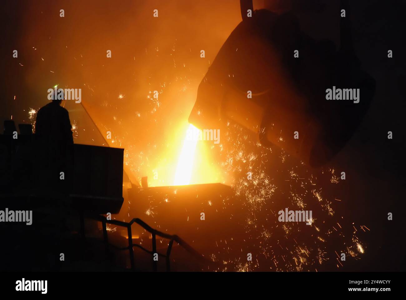 Das Bild zeigt eine dramatische Szene in einer Gießerei oder einem Stahlwerk, bei der geschmolzenes Metall aus einer großen Pfanne in eine Form oder gegossen wird Stockfoto
