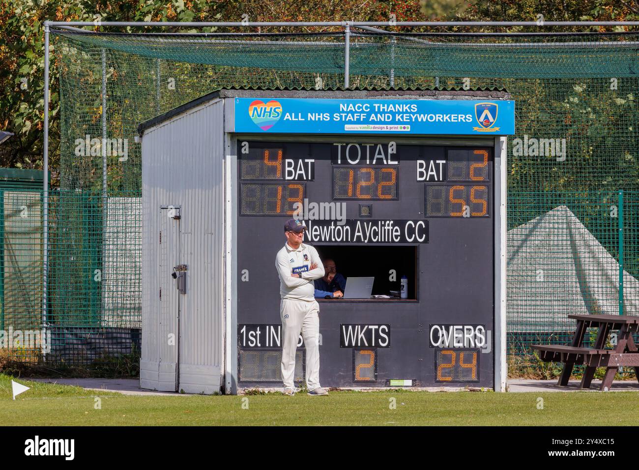 Der Newton Aycliffe Cricket Club war an einem sonnigen Samstagnachmittag Gastgeber des Middlesborough Cricket Club. Fielder steht auf der Grenze vor der Anzeigetafel Stockfoto