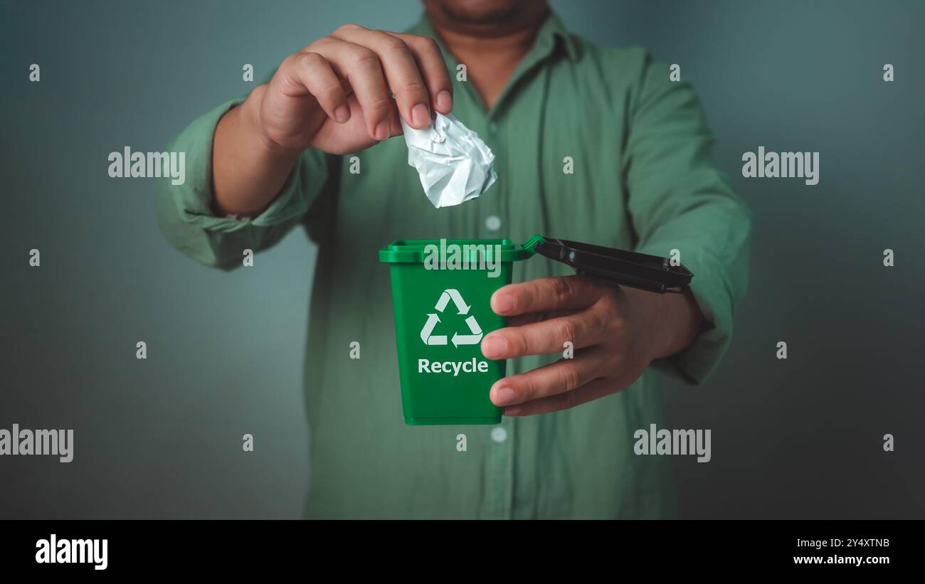 Mann trägt ein grünes Hemd, der Recyclingbehälter hält und das Papier in den Abfallbehälter wirft, Abfallsortierung und Nachhaltigkeitskonzept, Recycling, nachhaltiges Leben Stockfoto