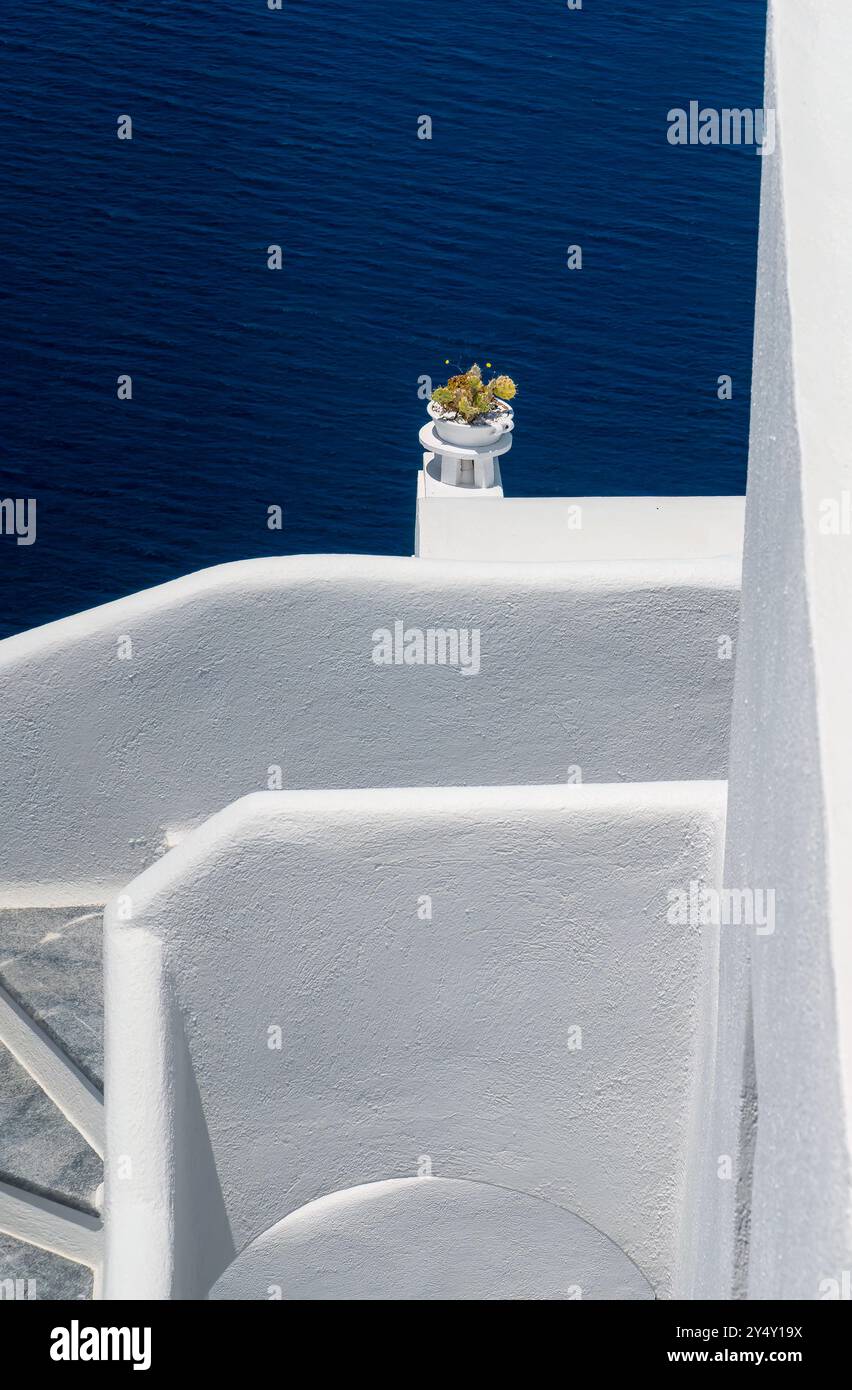 Traditionelle weiß getünchte Hauswand mit Kakteen in weißen Fliesen und tiefblauem Meer im Hintergrund. Santorin, Griechenland Stockfoto