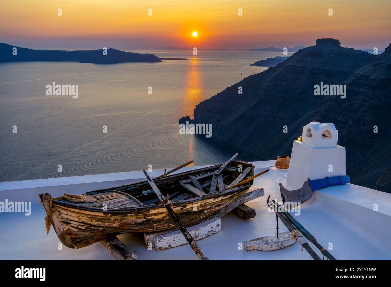 Sonnenuntergang mit einem alten Fischerboot Touristenattraktion auf dem glitzernden weißen Dach eines Höhlenhauses. Fira Village, Santorini oder Thira Island, Griechenland. Stockfoto