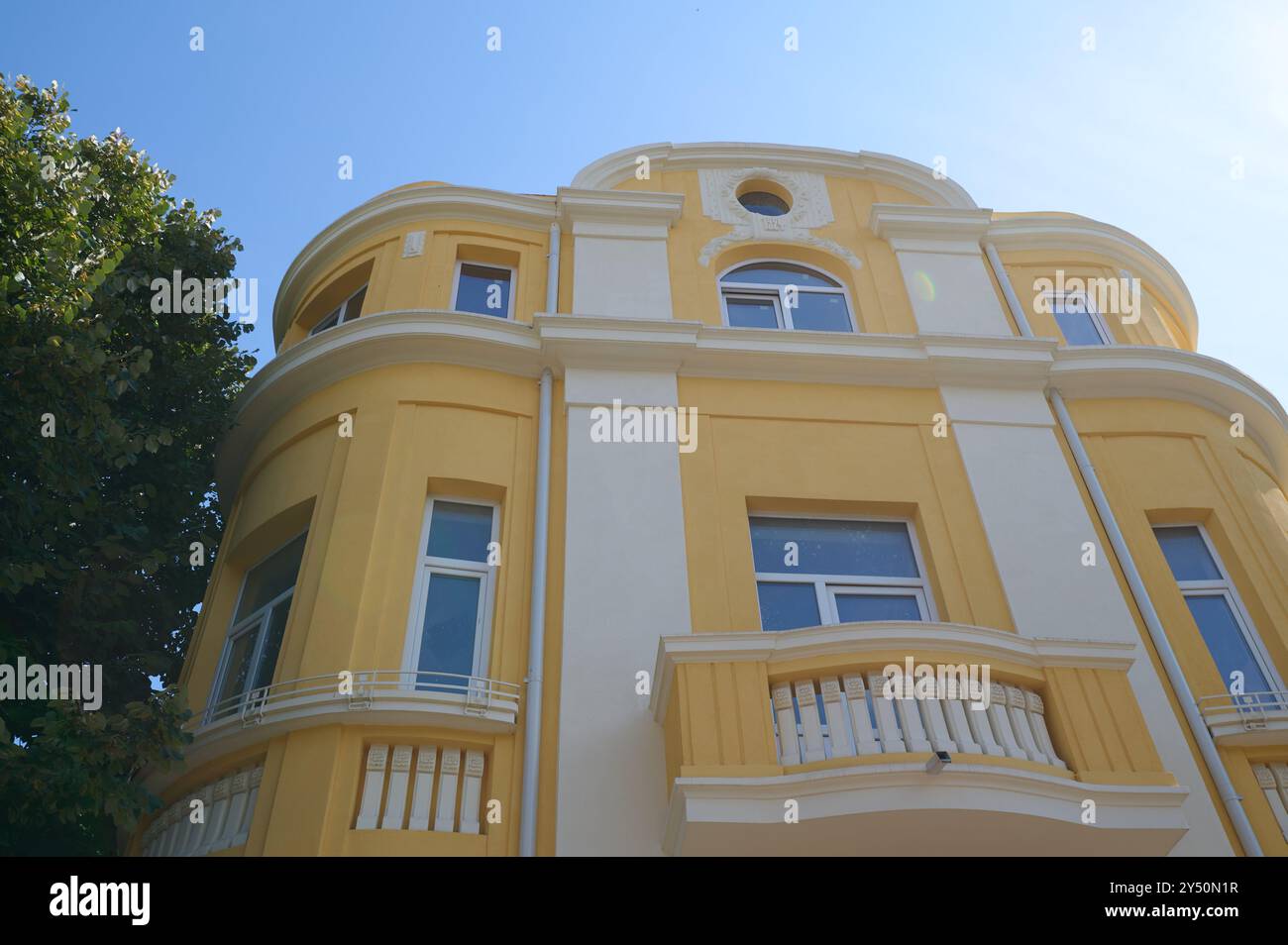 Architektonische Schönheit eines lebhaften gelben Gebäudes mit abgerundeten Kanten in einem sonnendurchfluteten Stadtgebiet Stockfoto