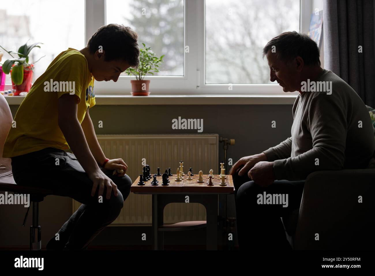 Junge spielt Schach mit seinem Großvater drinnen an einem ruhigen Nachmittag im Winter Stockfoto