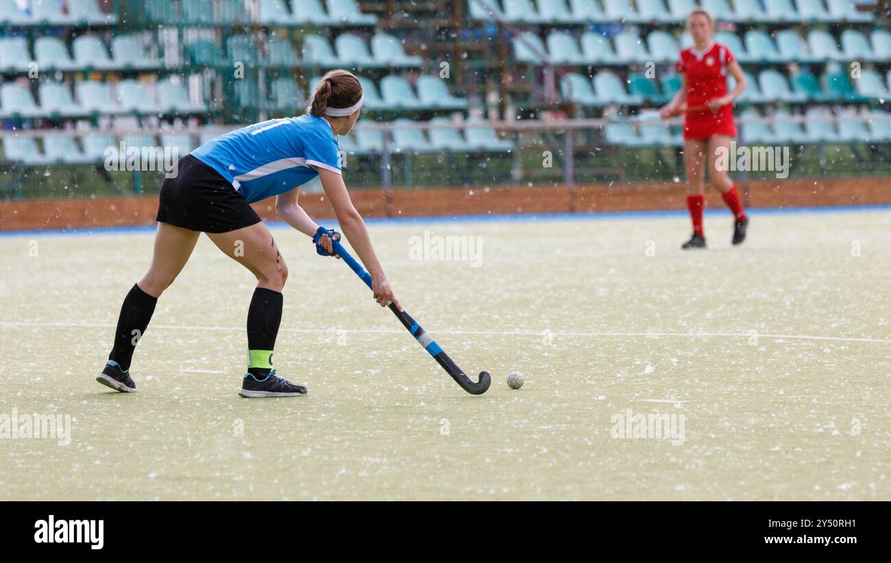 Eine Hockeyspielerin führt den Ball während eines Spiels in einem Stadion, das mit Pappelfluff bedeckt ist Stockfoto