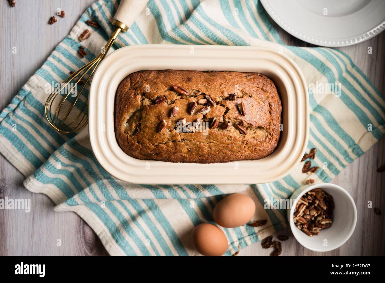 Bananenbrot auf einem gestreiften Handtuch mit Bananen und Eiern in der Nähe Stockfoto