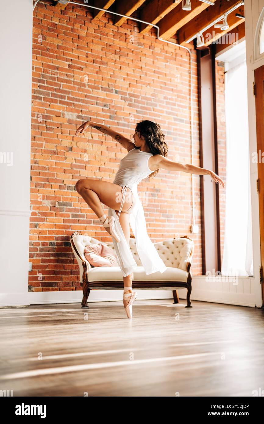 Balletttänzerin in Mittelstellung mit ausgestreckten Armen in einem Loft-Studio Stockfoto