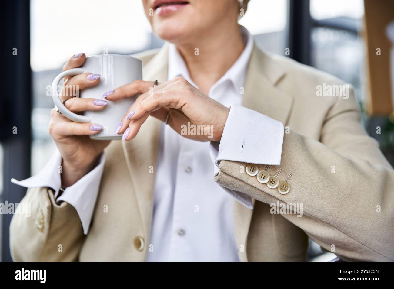 Eine stilvolle Frau schlürft Kaffee und zeigt ihre schicken Nägel und eine entspannte Atmosphäre. Stockfoto