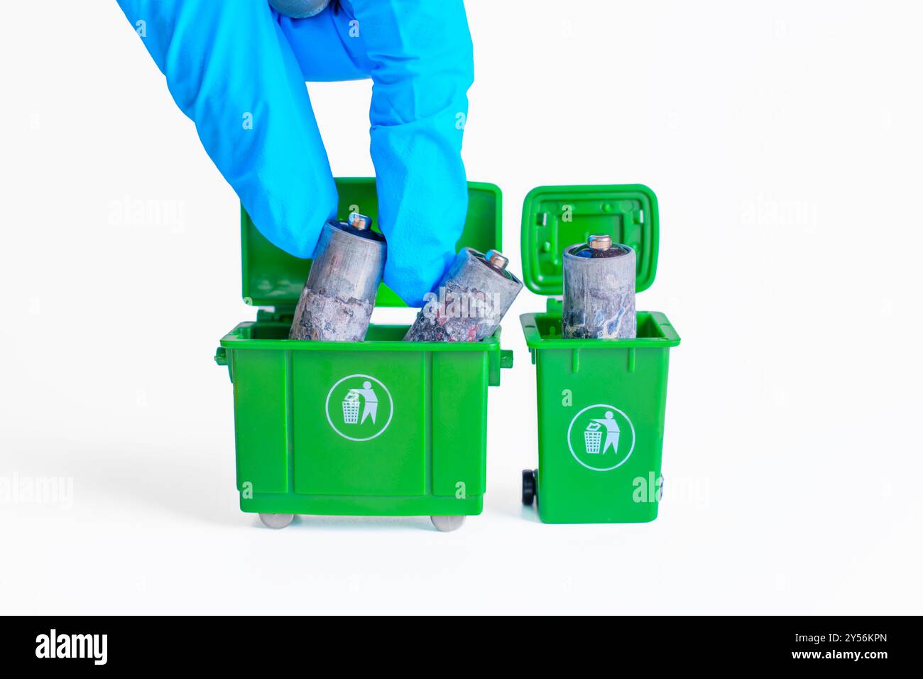 Miniaturszene eines Handschuhs, der stark oxidierte Batterien in grüne Mülltonnen entsorgt, um die sichere Entsorgung zu verdeutlichen. Stockfoto