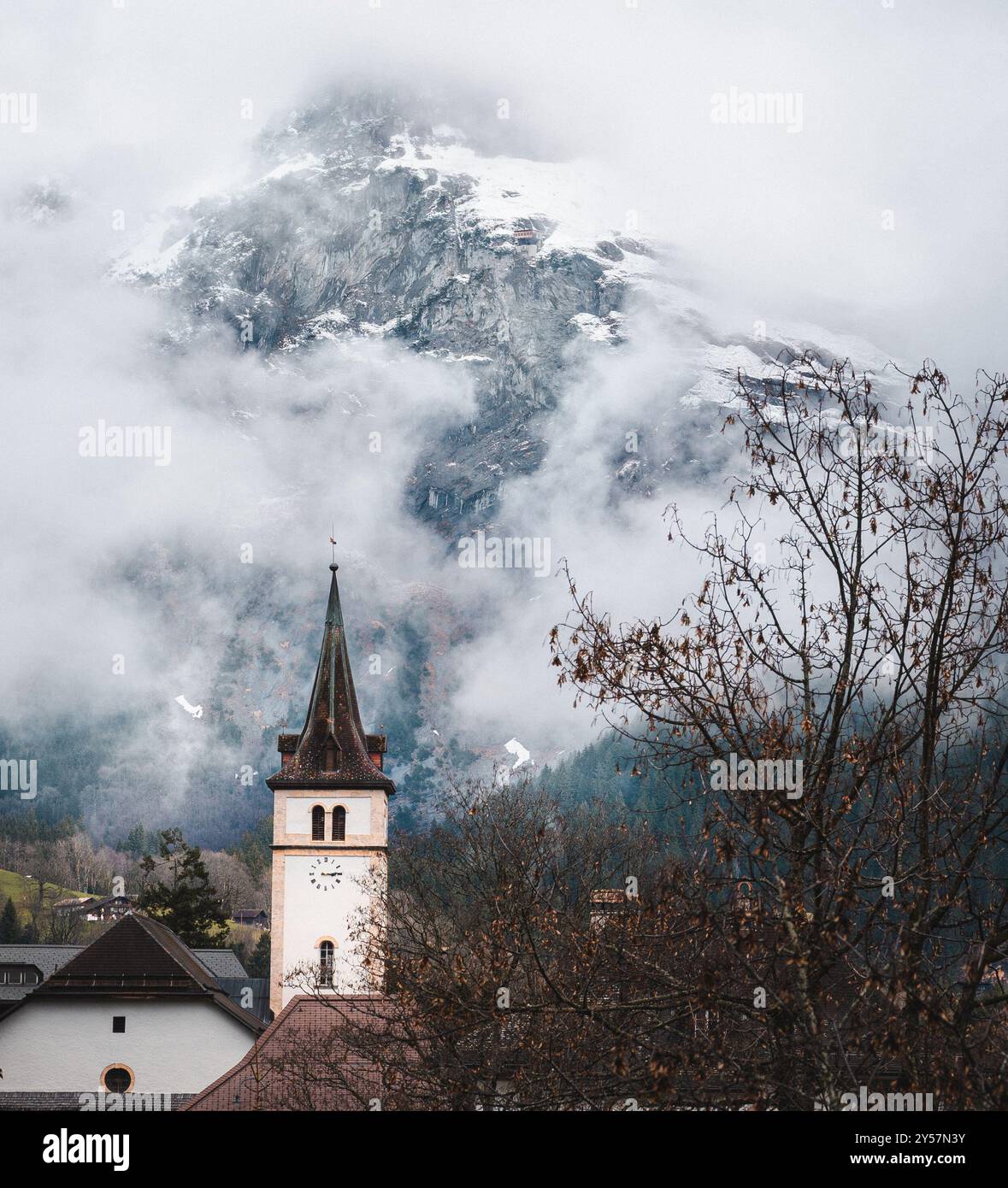 Ein Kirchturm in der Schweiz, umgeben von niedrigen Wolken und Nebel. Die Berge sind im Hintergrund durch den Dunst sichtbar. Stockfoto