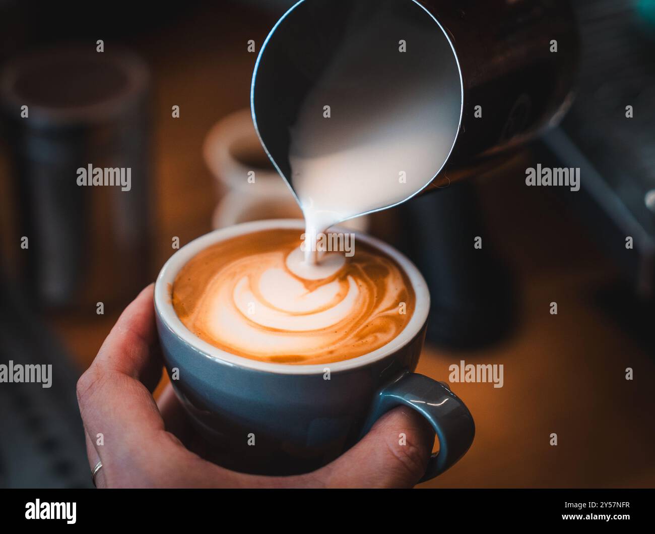 Ein Kaffee, der in einem Café in Melbourne, Australien, in eine blaue Tasse gegossen wird. Der Barista macht Latte Art mit aufgeschäumter Milch. Nahaufnahme. Stockfoto