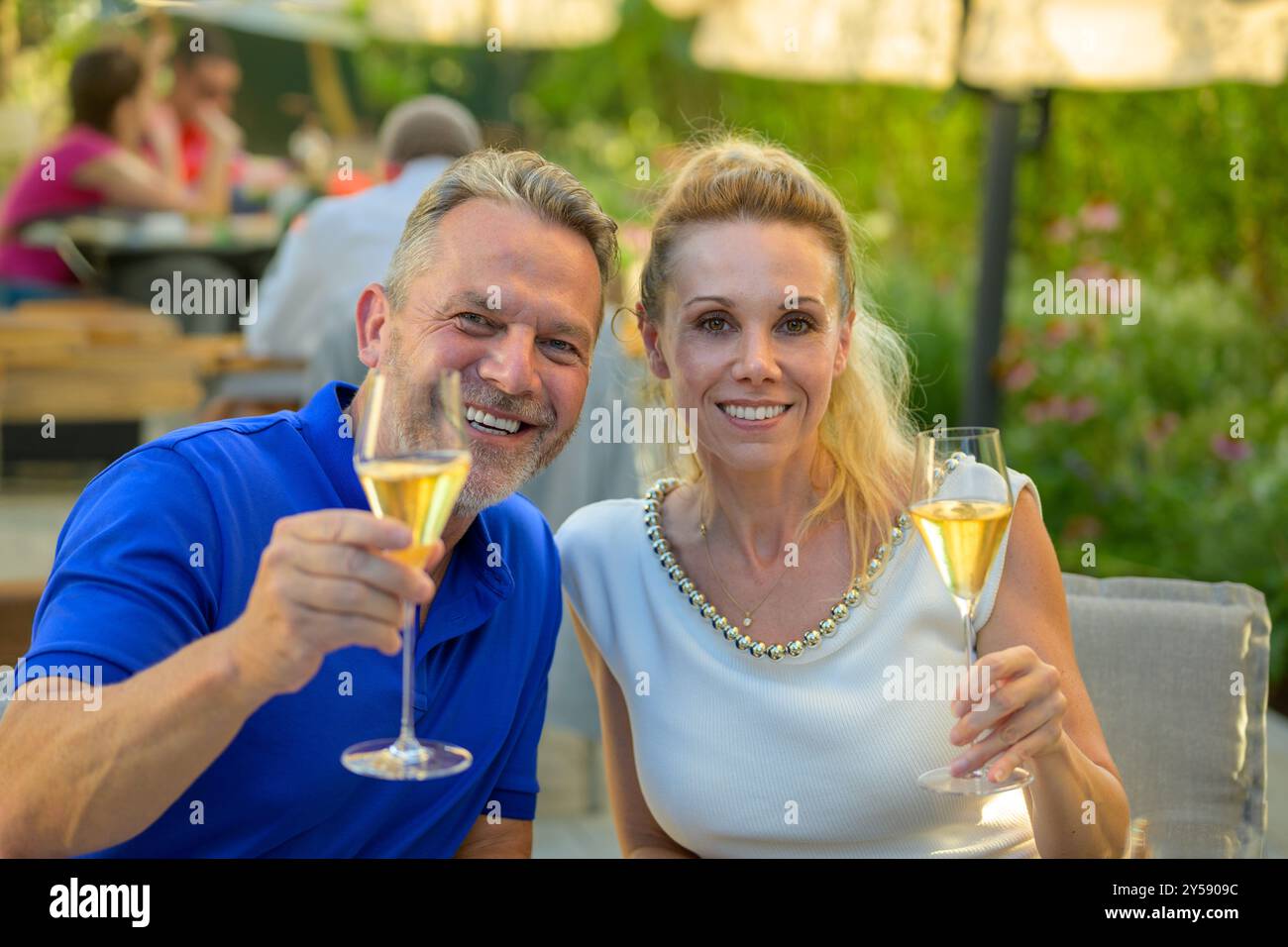 Ein fröhliches Paar genießt einen Toast mit Sektgläsern, während es draußen in einer entspannten und geselligen Umgebung sitzt. Stockfoto