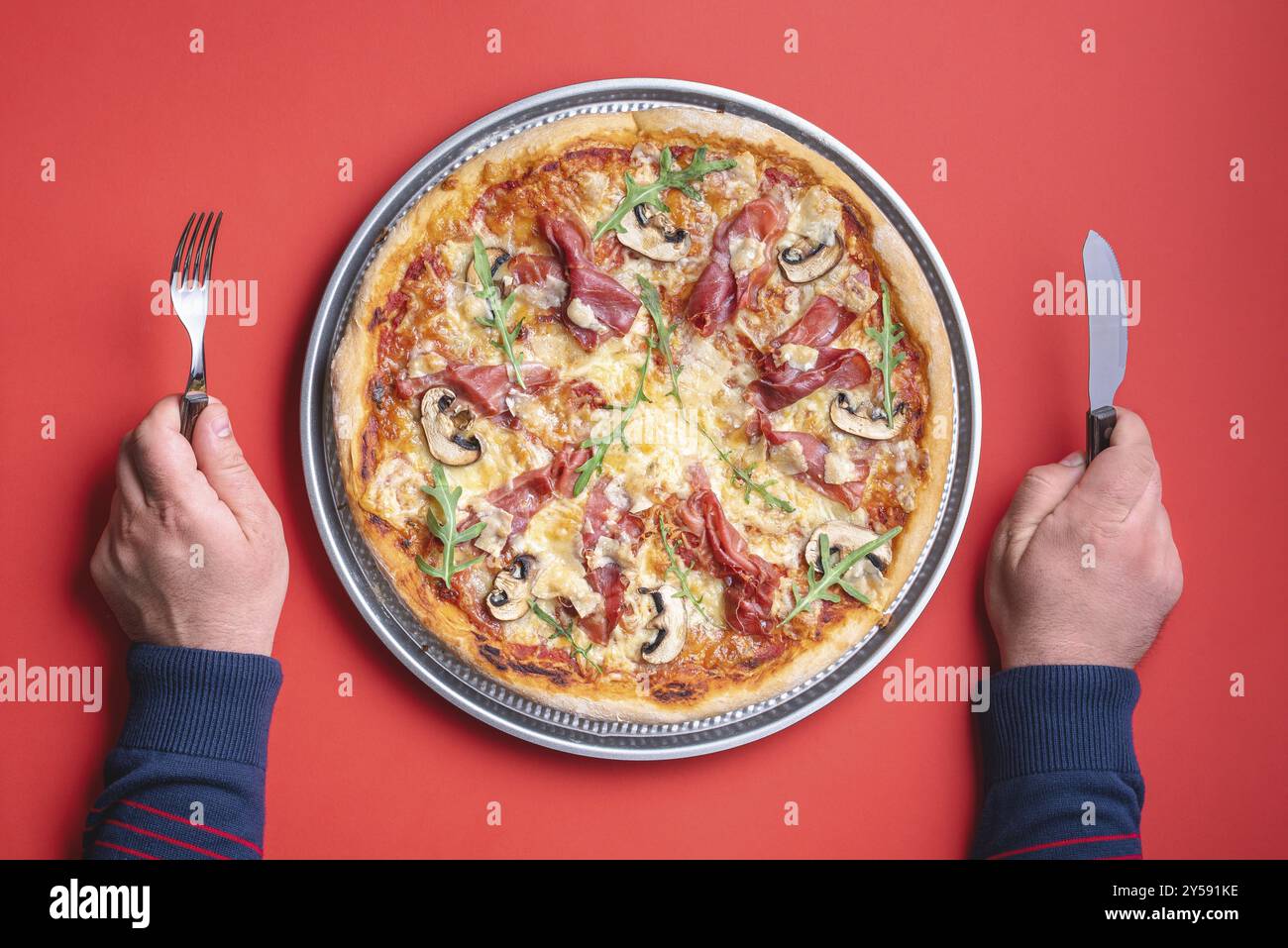 Ein Mann, der bereit ist, eine köstliche hausgemachte Schinken-Pizza zu essen. Blick von oben mit einer Prosciutto-Pizza auf rotem Hintergrund Stockfoto