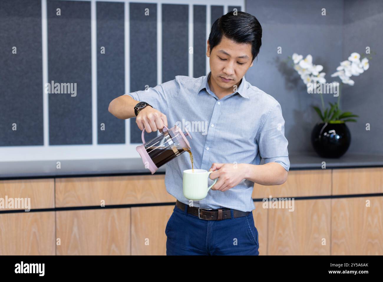 Kaffee aus der französischen Presse in den Becher gießen, asiatischer Mann in Geschäftskleidung in der Büroküche Stockfoto