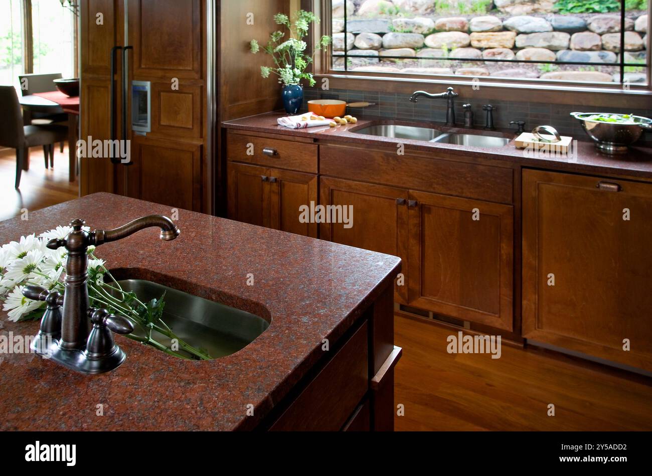 Kleines Barwaschbecken auf Kücheninsel mit Schränken und großem Waschbecken im Hintergrund Stockfoto