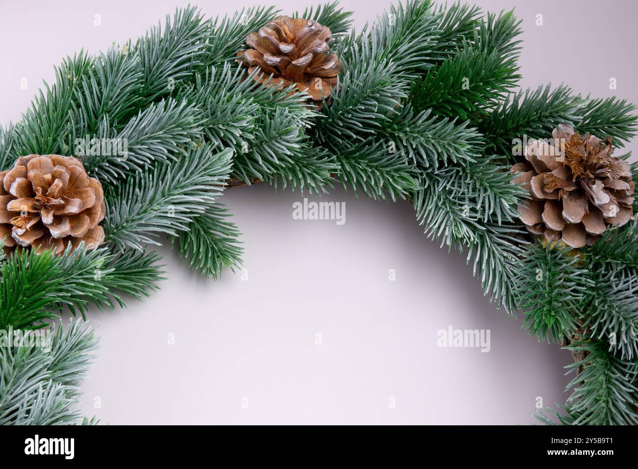 Eine Nahaufnahme eines grünen Kieferkranzes mit braunen Kiefernzapfen. Der Kranz ist halbkreisförmig auf weißem Hintergrund angeordnet. Stockfoto