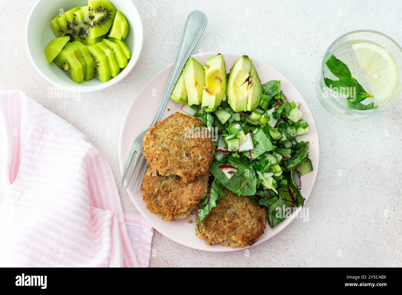 Quinoa-Schnitzel und gemischter Salat mit Avocado und Radieschen, Kiwi und Wasser mit Zitrone, köstliches herzhaftes Frühstück, veganer Lunch-Teller Stockfoto