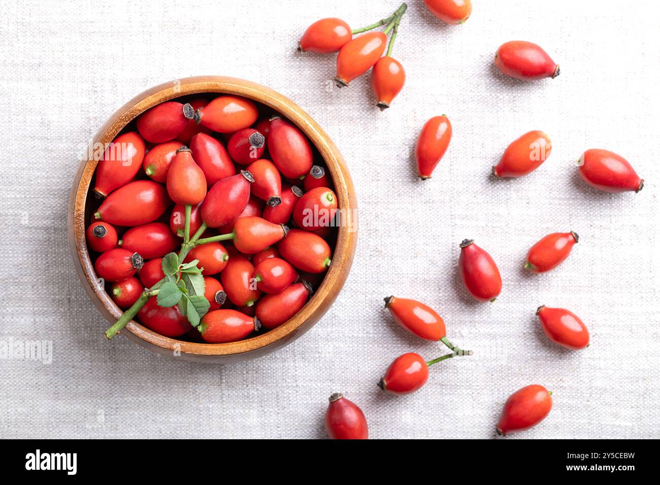 Frische Hüftrosen in einer Holzschale auf Leinen. Auch Rosenhau oder Rosenhep, intensive rote reife Früchte, die für Kräutertees und Marmelade verwendet werden und roh gegessen werden können. Stockfoto