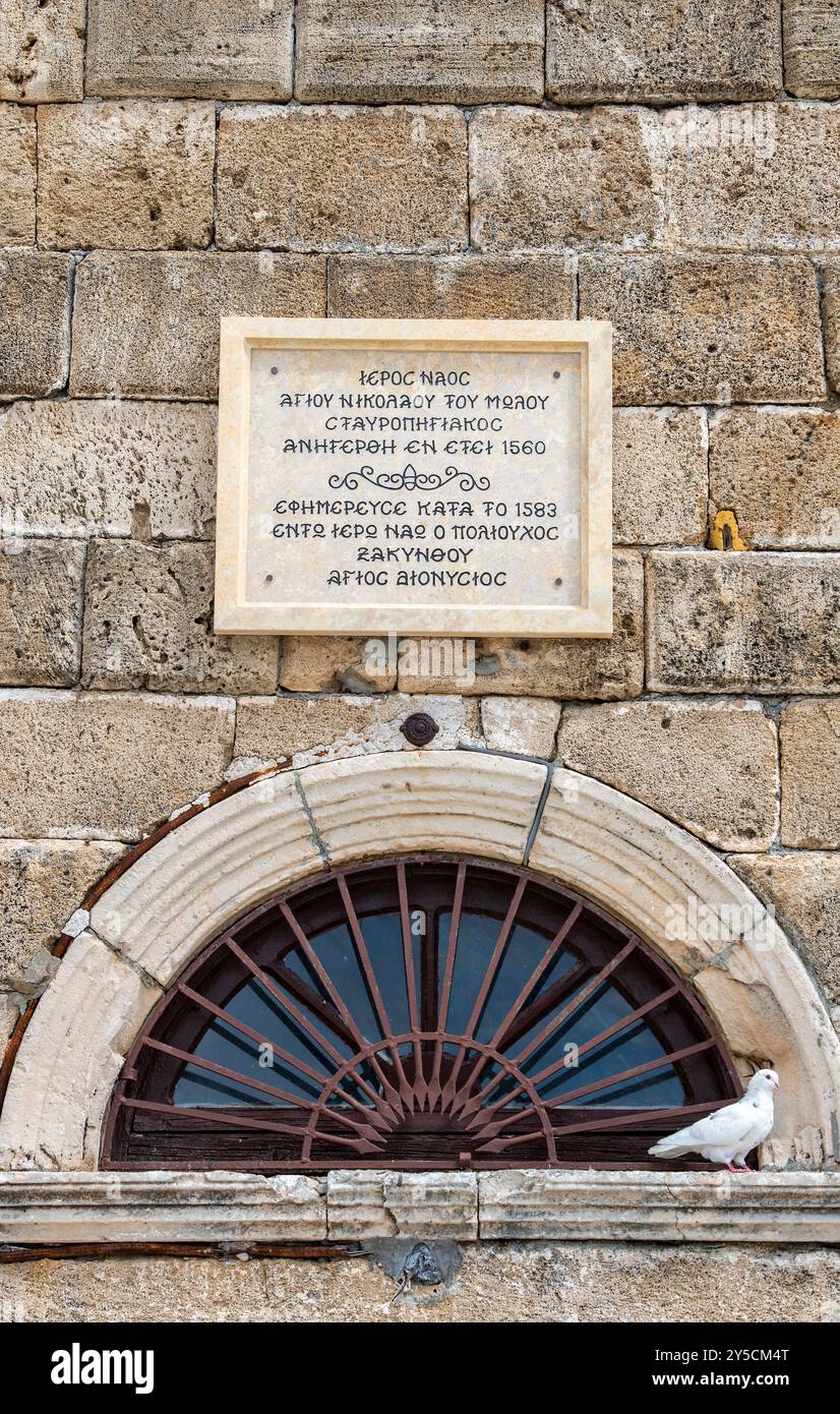 Weiße Taube neben einem bogenförmigen Fenster und einer Gedenktafel über der Tür von Agios Nikolaos von Molos auf dem Solomos-Platz auf der Insel Zante Stockfoto