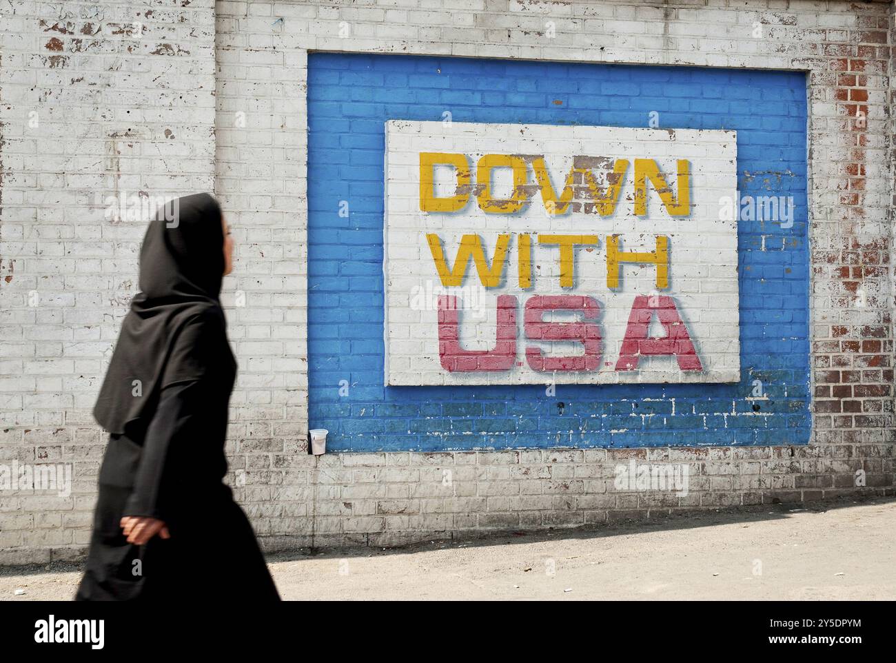 Schwarzer Schleier mit muslimischer Frau, die an antiamerikanischen Wandgemälden vor der alten amerikanischen Botschaft in teheran, iran, vorbeiläuft Stockfoto