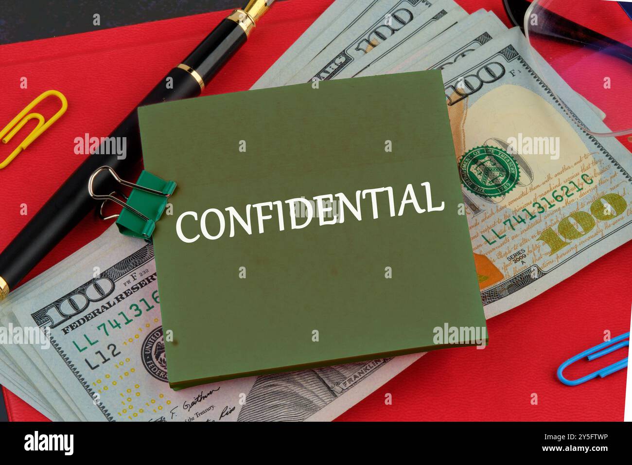VERTRAULICHE Buchstaben auf einem grünen Aufkleber auf dem Hintergrund von Dollarscheine auf dem roten Buch Stockfoto