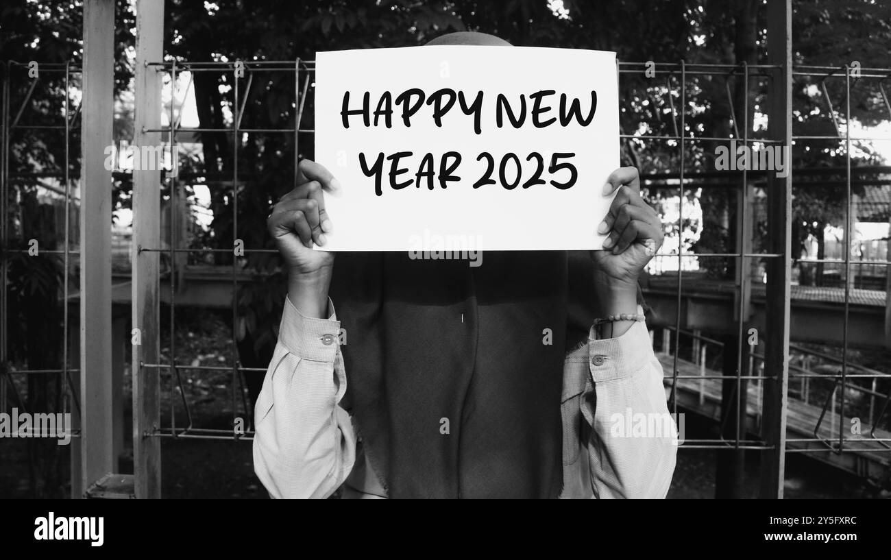 Ein Mädchen, das einen Happy New Year 2025-Schein hält. Neujahrskonzept mit Typografie 2025. Motivierende Worte zur Begrüßung des neuen Jahres 2025 Stockfoto