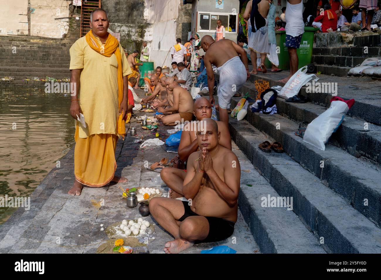 Ein Hindupriester (l), der Riten für verstorbene Verwandte von Hindumenschen durchführt, letztere mit rituell rasierten Köpfen; im heiligen Banganga Tank, Mumbai, Ind Stockfoto