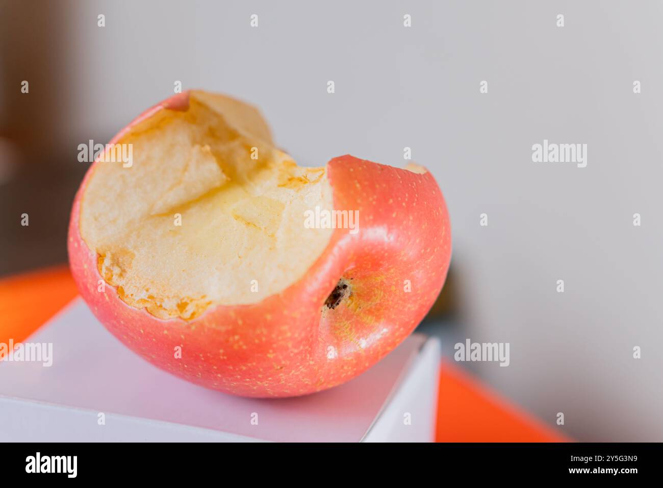 Ein teilweise gegessen roter Apfel, der auf einer weißen Oberfläche liegt und sein saftiges Inneres und seine lebendige Haut zeigt. Der Hintergrund ist leicht verschwommen und betont Stockfoto