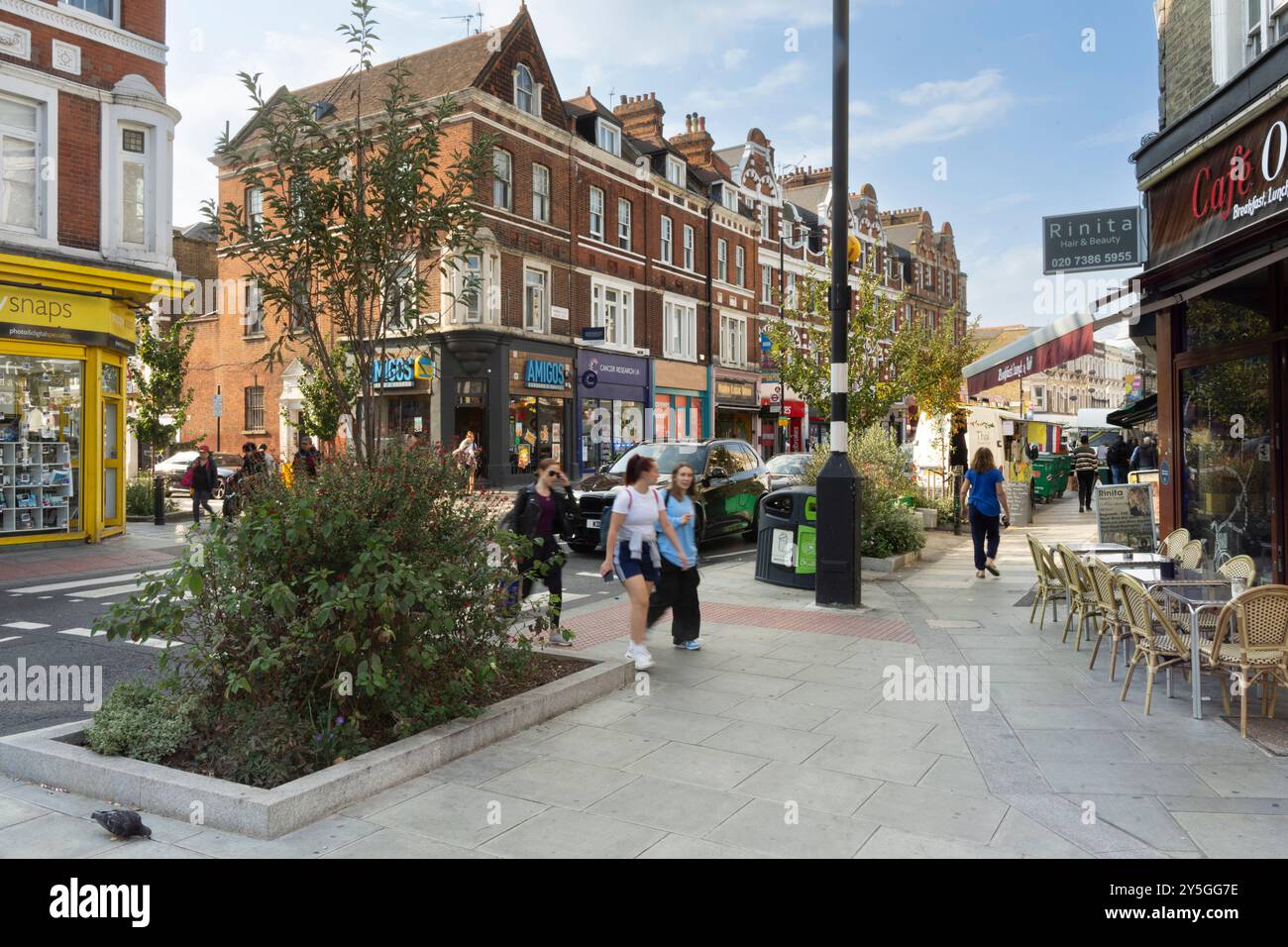 Fußgänger laufen auf einer Straße in London, wahrscheinlich in der Nähe einer Ecke einer Straße mit einem gelben Geschäft namens 'Snaps' und einem Restaurant namens 'Amigos'. Stockfoto