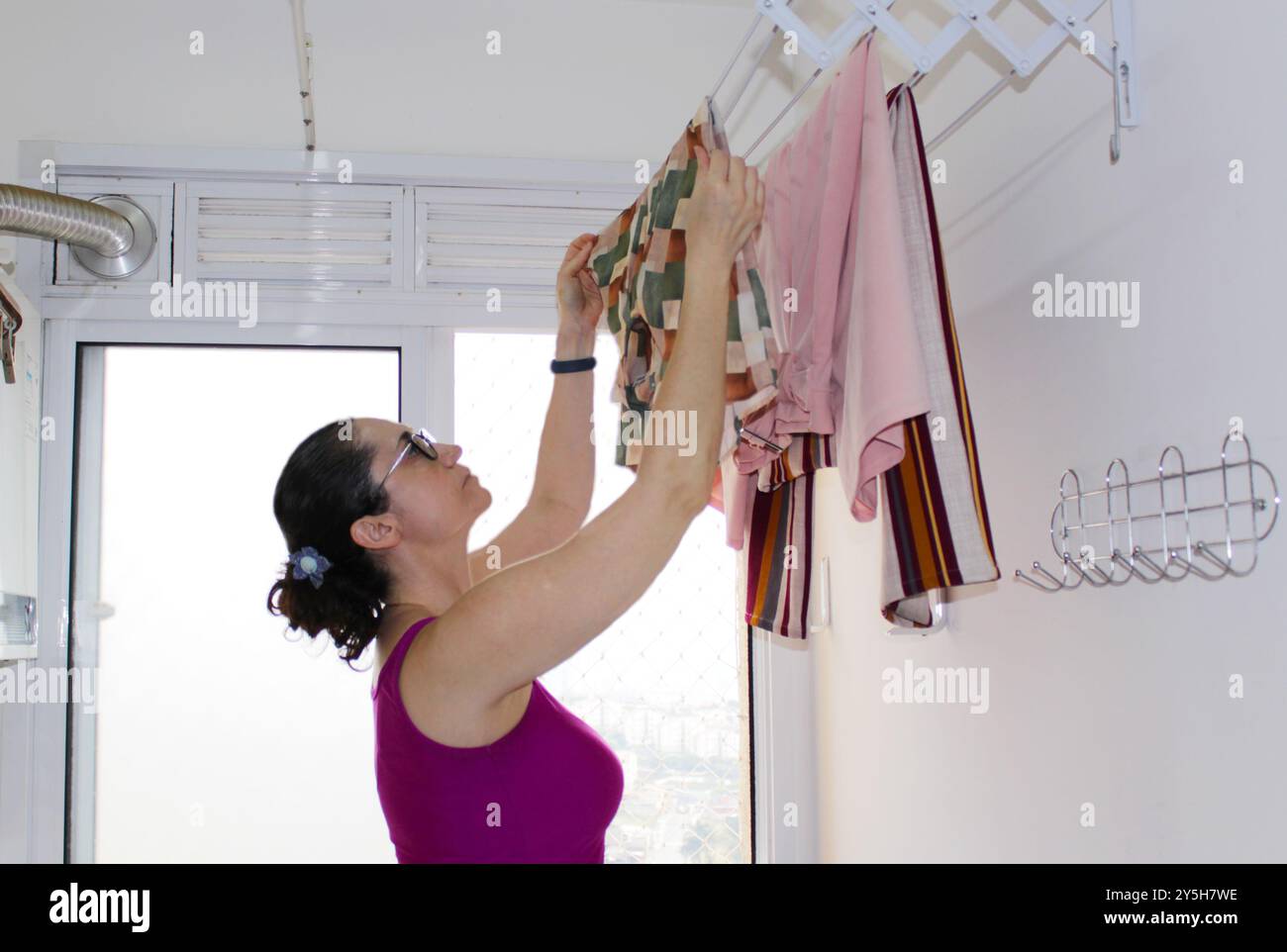 Die brünette Hausfrau in Brasilien macht Wäsche in einer winzigen Wohnung. Kaukasische Dame bei Hausaufgaben. Weiße Frau, die gewaschene Kleidung an der Wäscheleine hängt Stockfoto