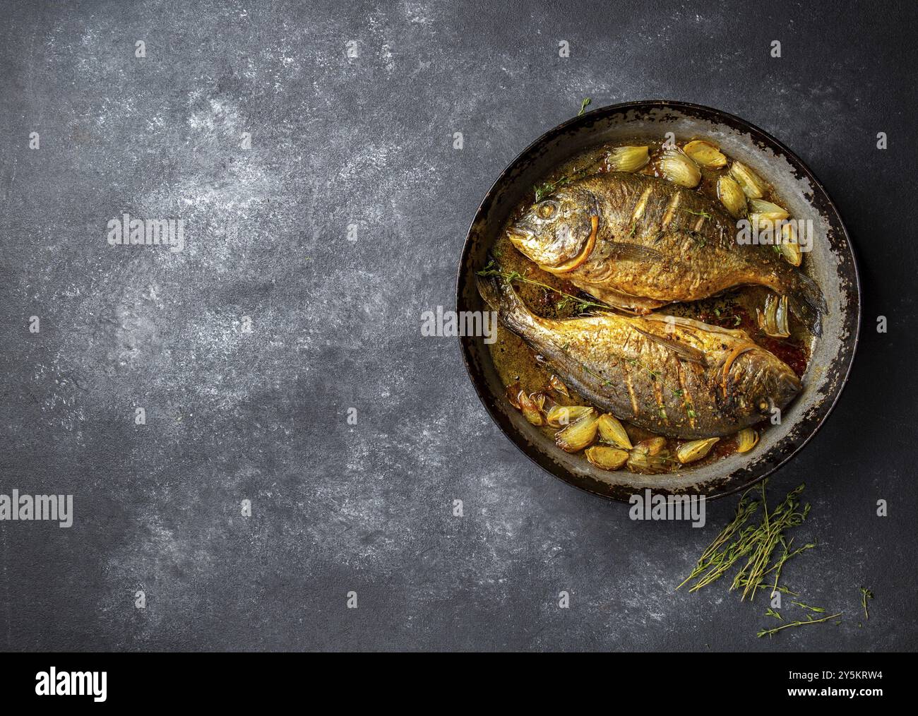 Gebackene Dorade oder Dorada mit Zwiebeln und Kräutern in der Pan auf dunklem Hintergrund Stockfoto