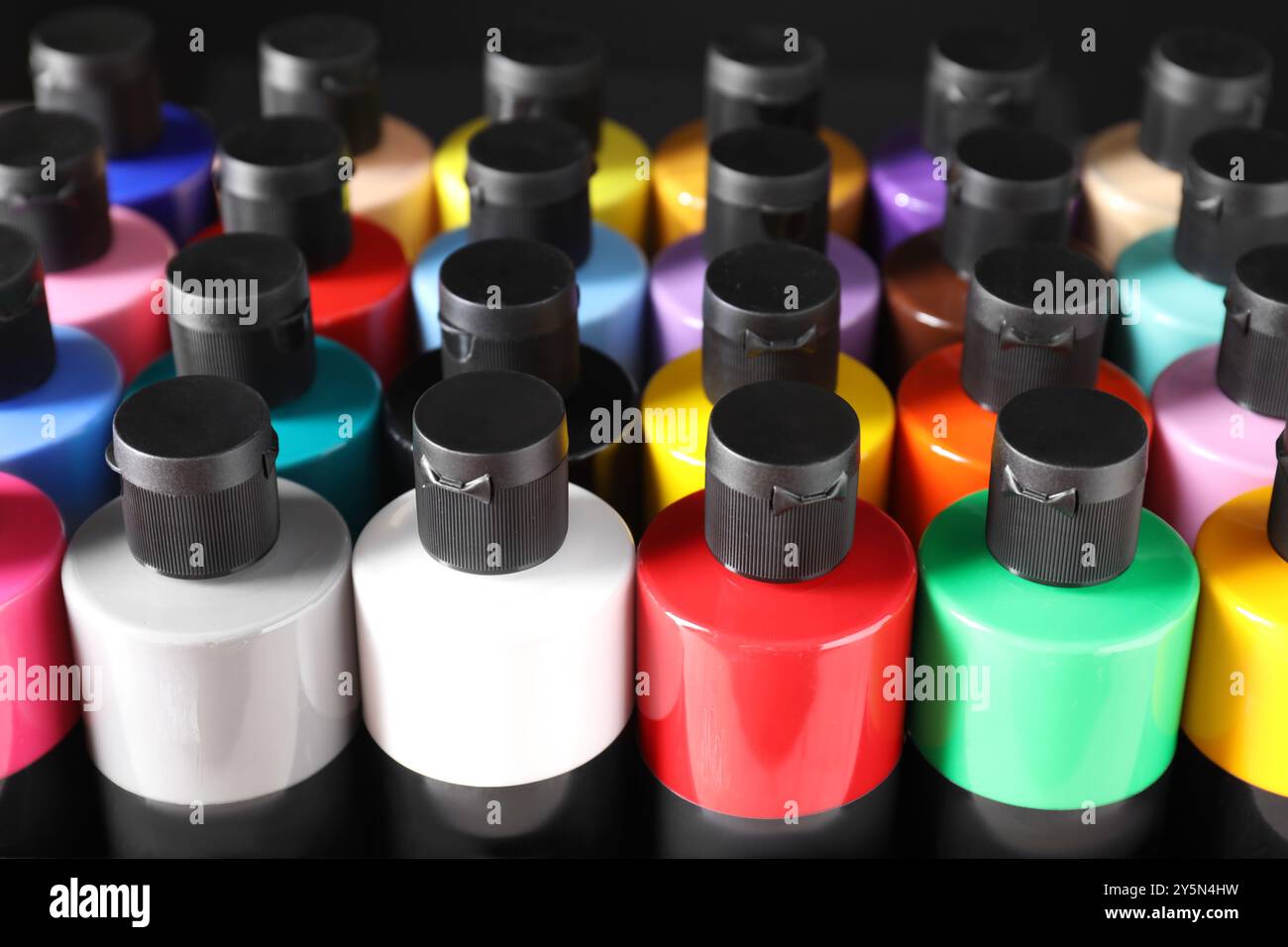 Acrylfarben in verschiedenen Farben in Flaschen vor schwarzem Hintergrund, Nahaufnahme Stockfoto