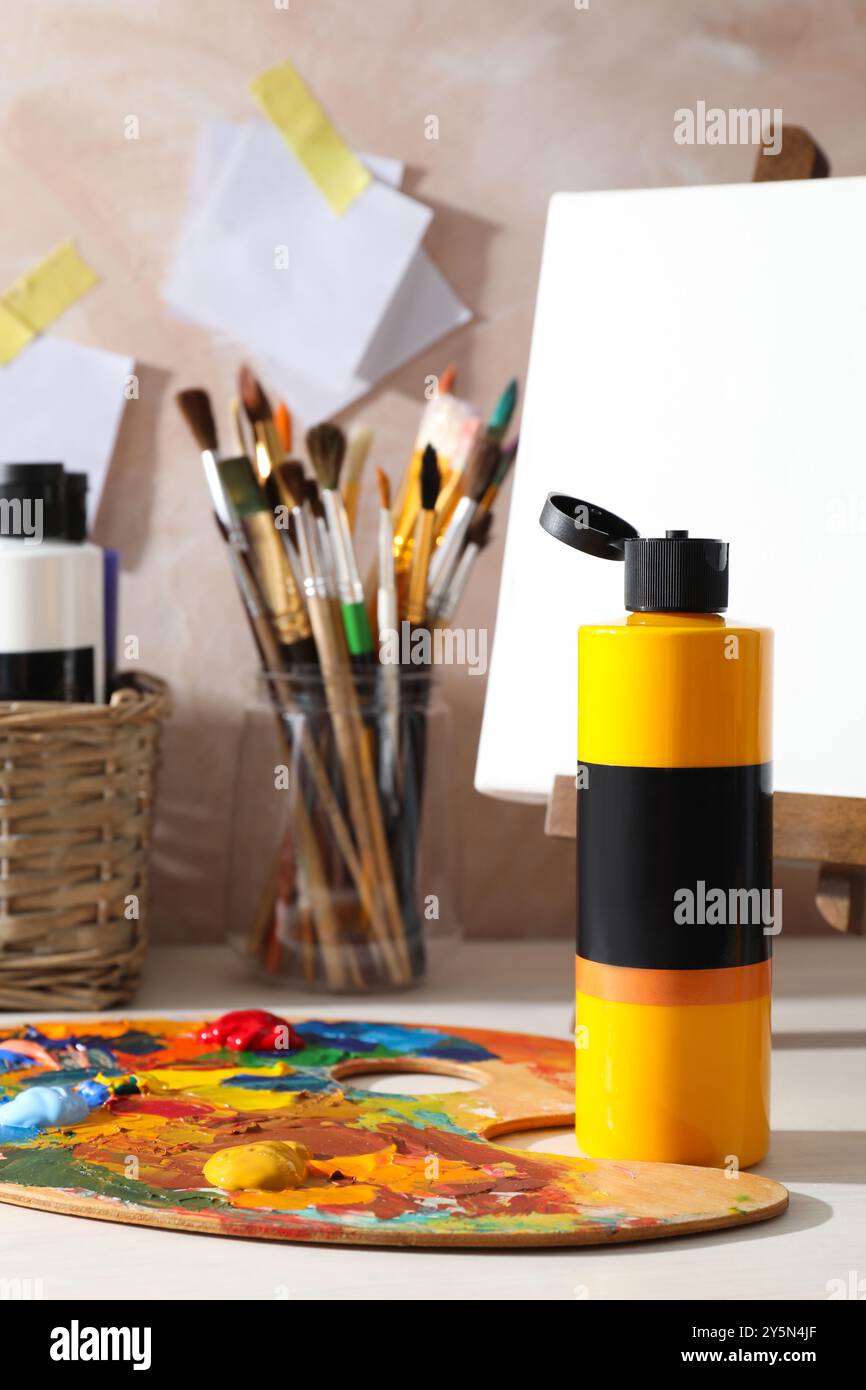 Orangefarbene Acrylfarbe in der Flasche, kleine Staffelei, Palette und Pinsel auf Holztisch drinnen Stockfoto