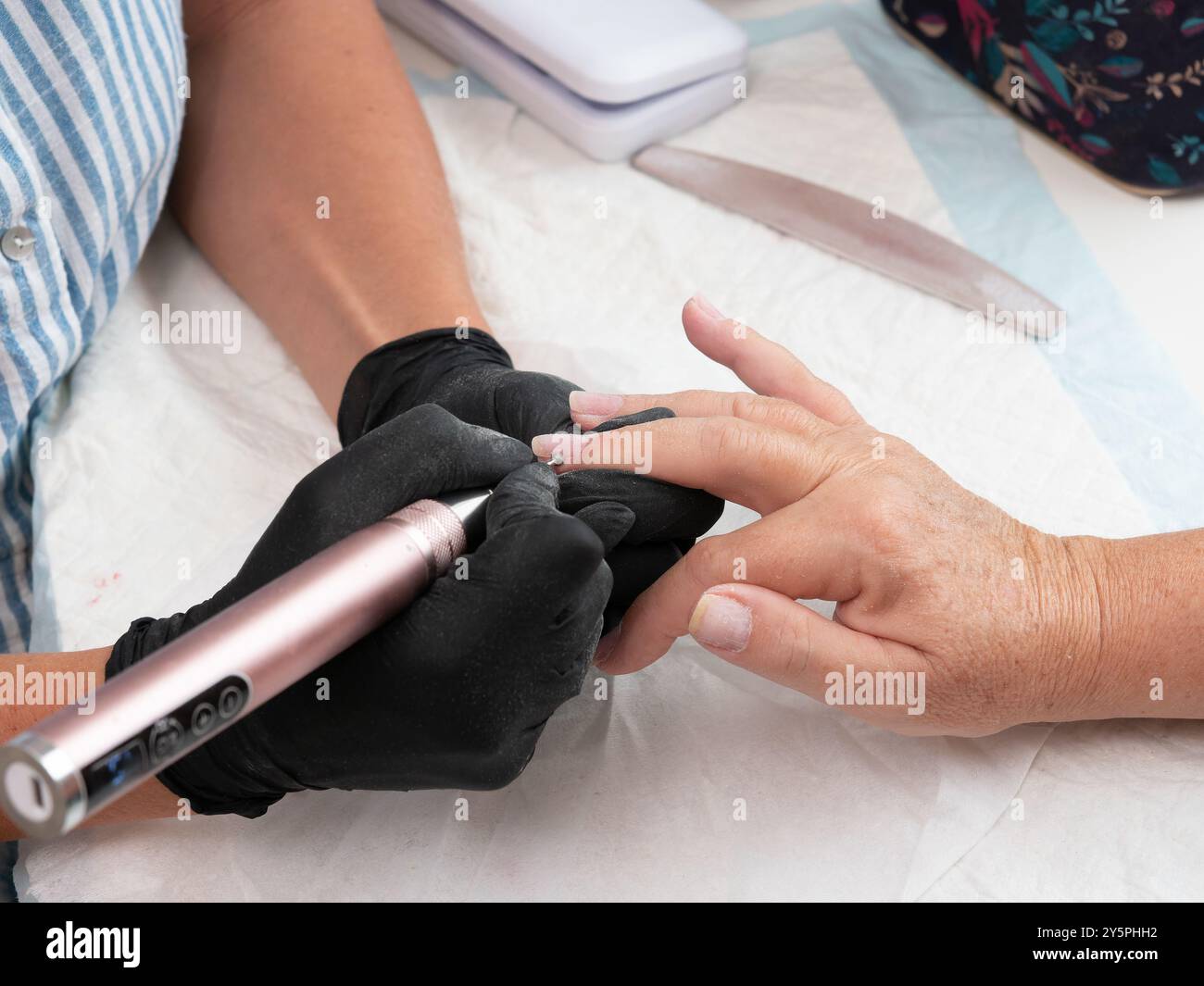 Eine Maniküre reinigt Nagelhaut und Farbreste von den Nägeln einer Frau mit einem elektrischen Nagelbohrer mit einer Kugelmühle. Stockfoto