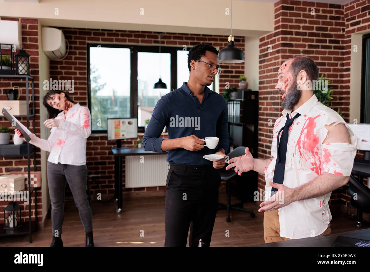 afroamerikanischer Regisseur am Set, der dem Schauspieler, der Zombie in Horrorfilmen darstellt, eine Anleitung gibt, während die Schauspielerin im Hintergrund Drehbücher liest. Filmemacher und Mann im Ghul-Kostüm planen Filmdreh Stockfoto