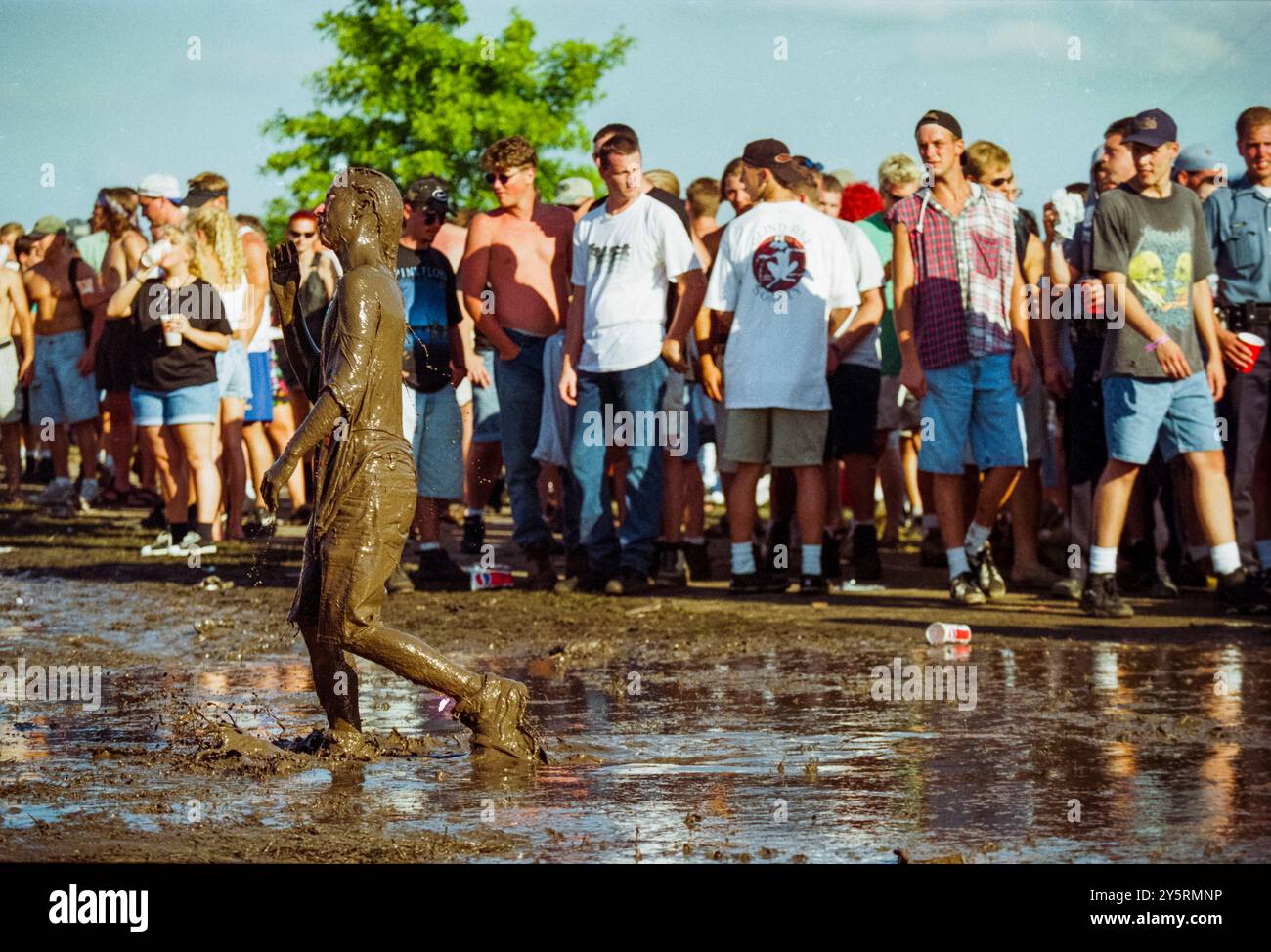 Am 11. Juli 1996 spaziert ein Festivalbesucher von Kopf bis Fuß durch das Gelände von Lollapalooza in Kansas City, während neugierige Zuschauer zusehen. Die matschigen Bedingungen wurden Teil des wilden und sorglosen Geistes des Festivals. Stockfoto