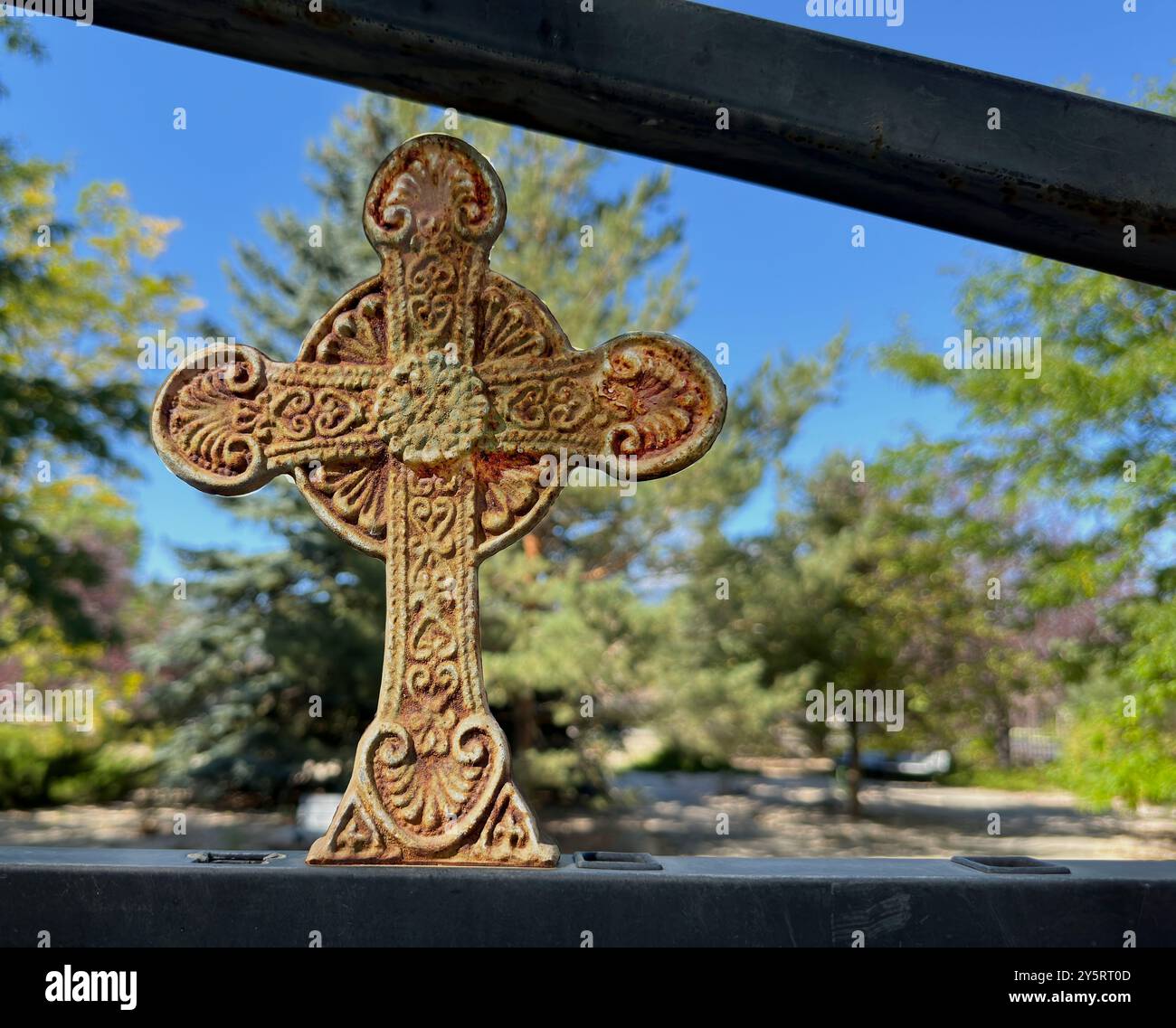 Ein altes eisernes Kreuz ziert einen Zaun im Gedenkgarten der Episcopal Church in Cody, Wyoming. Patina, Rost und ein altes künstlerisches Design repräsentieren die trinity. Stockfoto