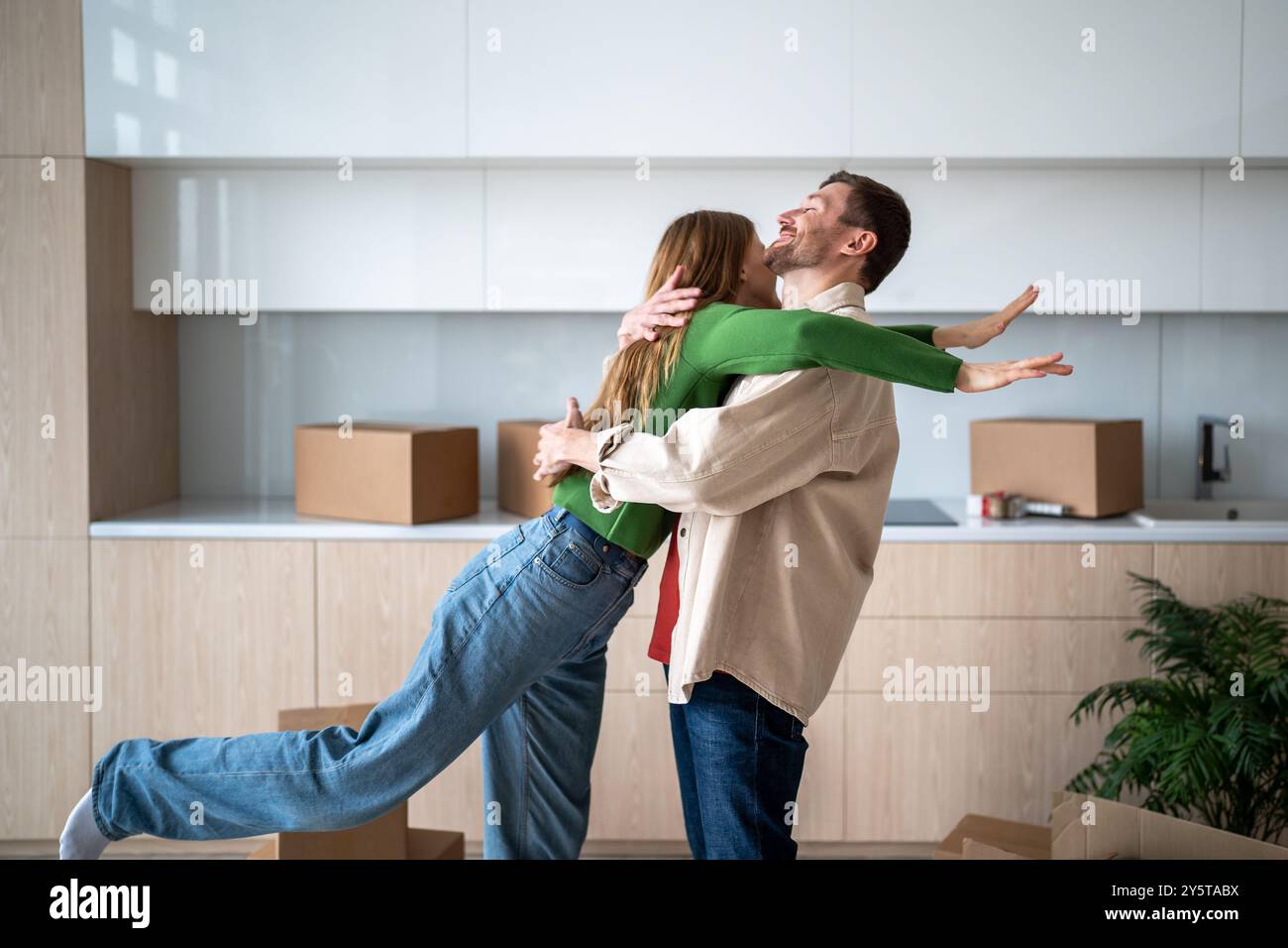 Glückliche Frau, die einen lächelnden, freudigen Ehemann am Umzugstag in ein neues Apartment, ein Haus, eine Wohnung umschließt Stockfoto