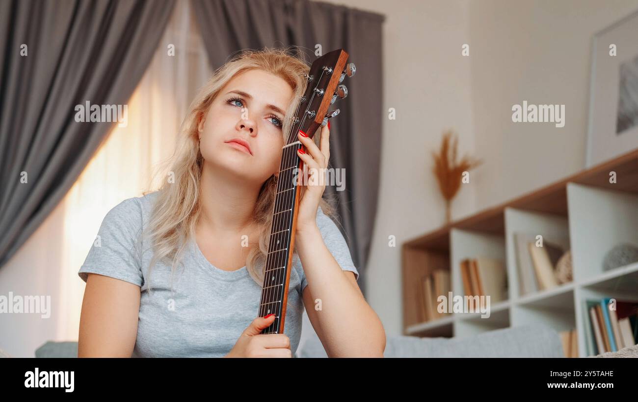 Verärgerte Frau. Gitarrenspieler. Depressive Stimmung. Traurige frustrierte Dame, die ein Musikinstrument hält, fühlt sich im Inneren des Zimmers romantisch und hell. Stockfoto