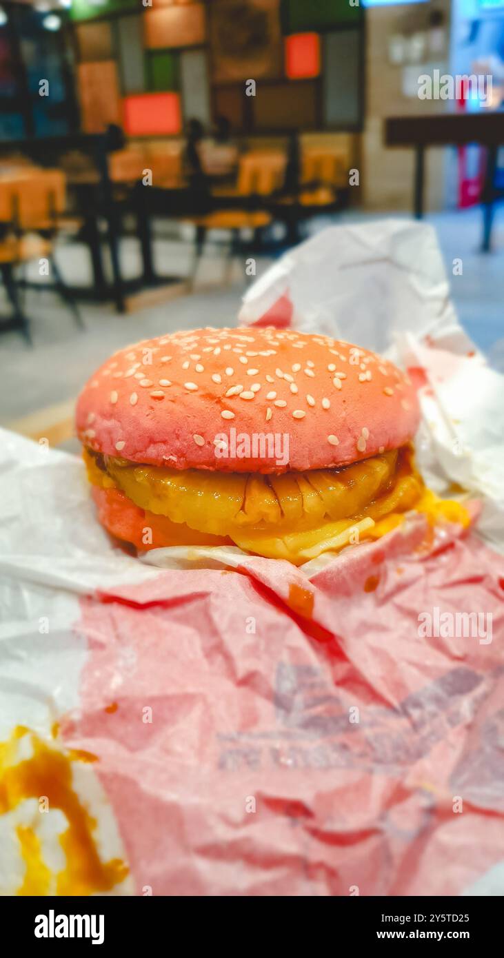 Der Biss stammt von einem köstlichen Cheeseburger. Pinker Burger mit Toppings innen. Stockfoto