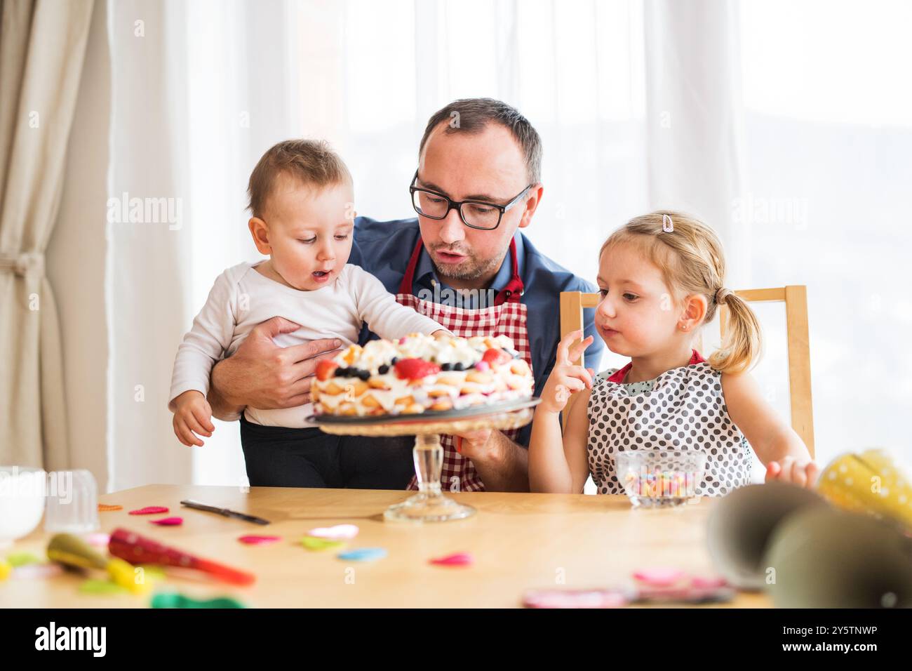 Dad, Kleinkind Sohn und Tochter bereiten Geburtstagsfeier vor, dekorieren Geburtstagstorte. Muttertagsgeschenk von Kindern. Stockfoto