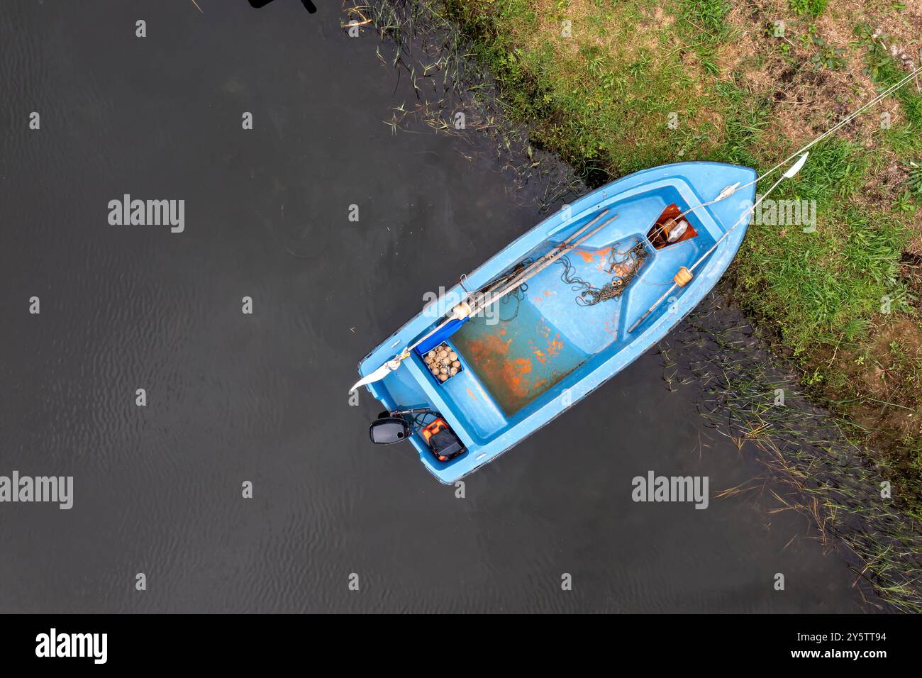 Ein kleines blaues Boot ruht ruhig am Ufer, was auf einen Tag zum Angeln hindeutet. Stockfoto