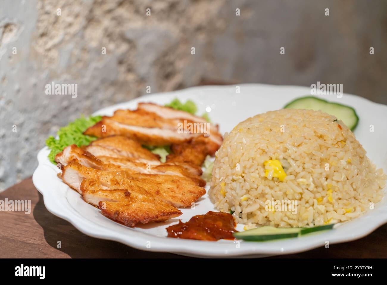 Nahaufnahme des frittierten Reis mit Hähnchenkotelett, Gurke, Salat Korallen und Chilisauce. Stockfoto