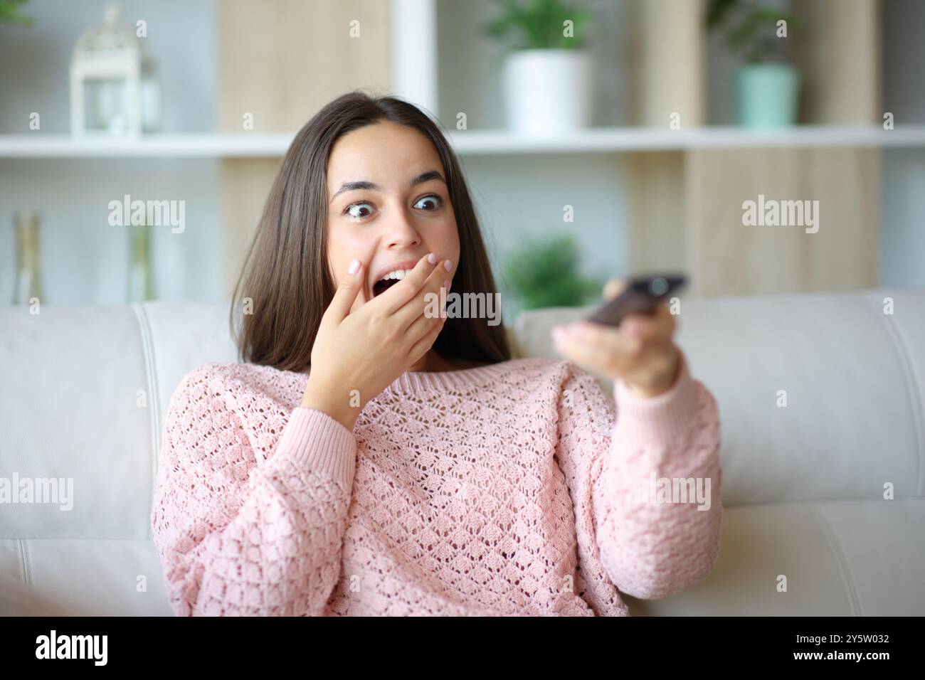 Staunte Frau, die zu Hause auf einem Sofa sitzt Stockfoto