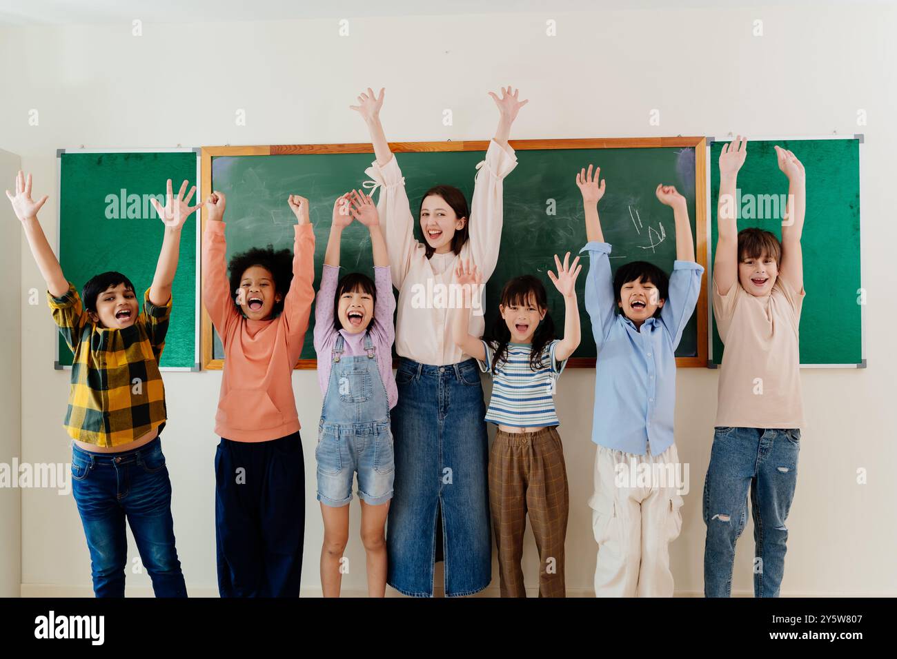 Vielfältige junge Schüler und begeisterter Pädagoge bringen während des Schultages Aufregung zum Ausdruck und fördern ein inklusives Lernumfeld Stockfoto