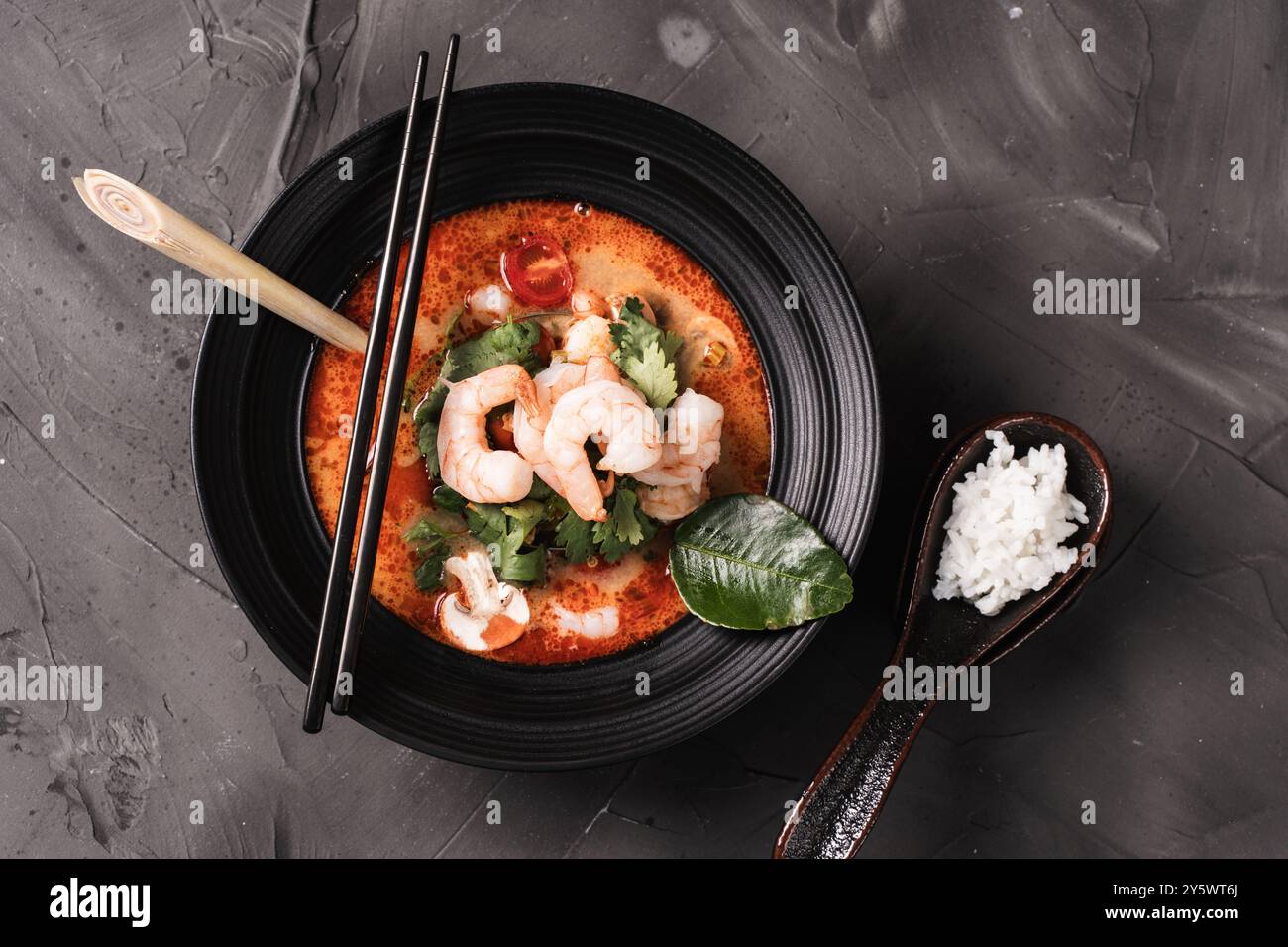 tom Yum Kung scharfe Thai-Suppe mit Garnelen in einer schwarzen Schüssel auf dunklem Steinhintergrund, Draufsicht, Kopierraum. Hochwertige Fotos Stockfoto
