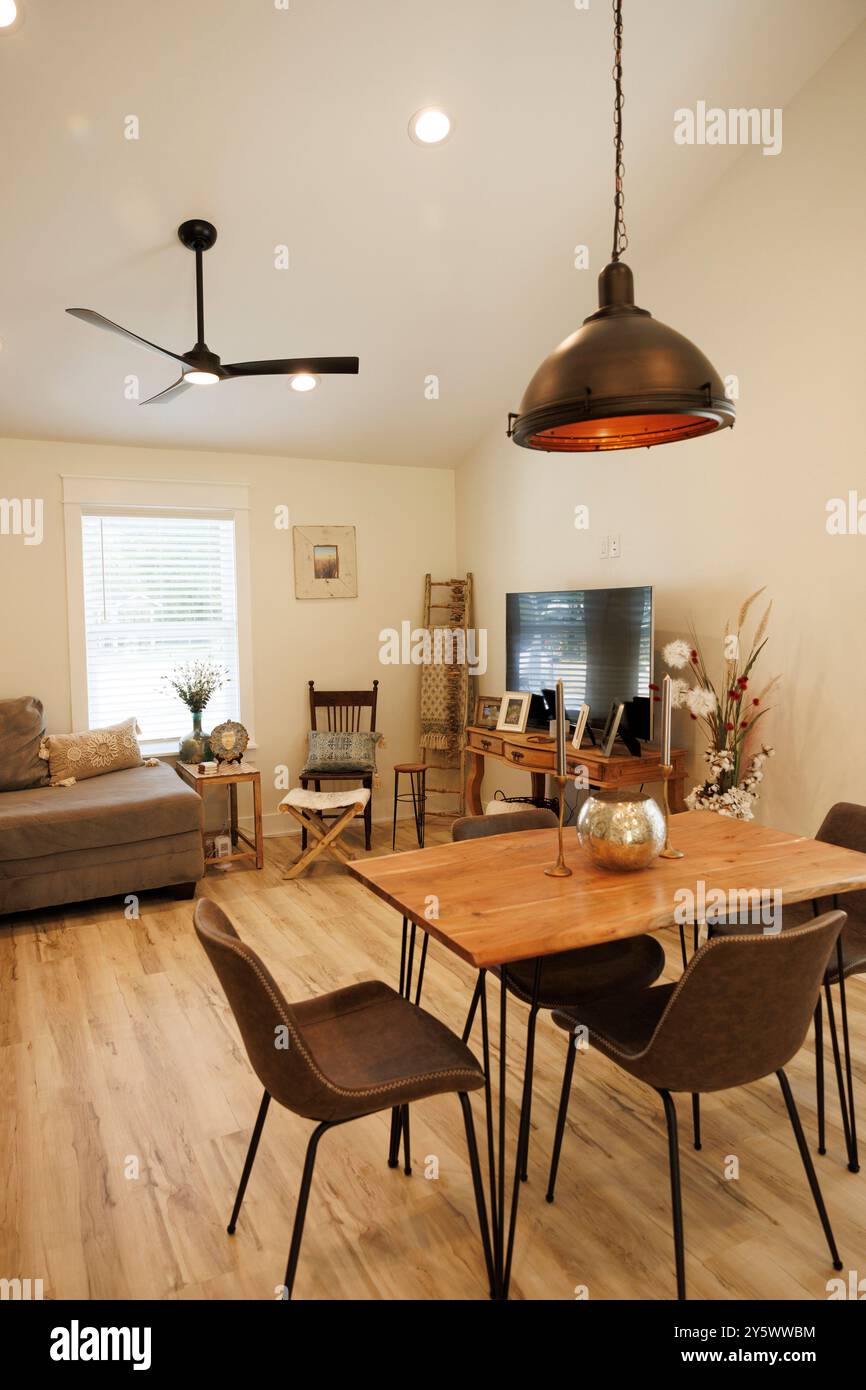 Modernes Wohnzimmer mit Holzesstisch, schwarzen Stühlen und Pendelbeleuchtung, ergänzt durch ein gemütliches Sofa und Fernseher, Florida, USA Stockfoto