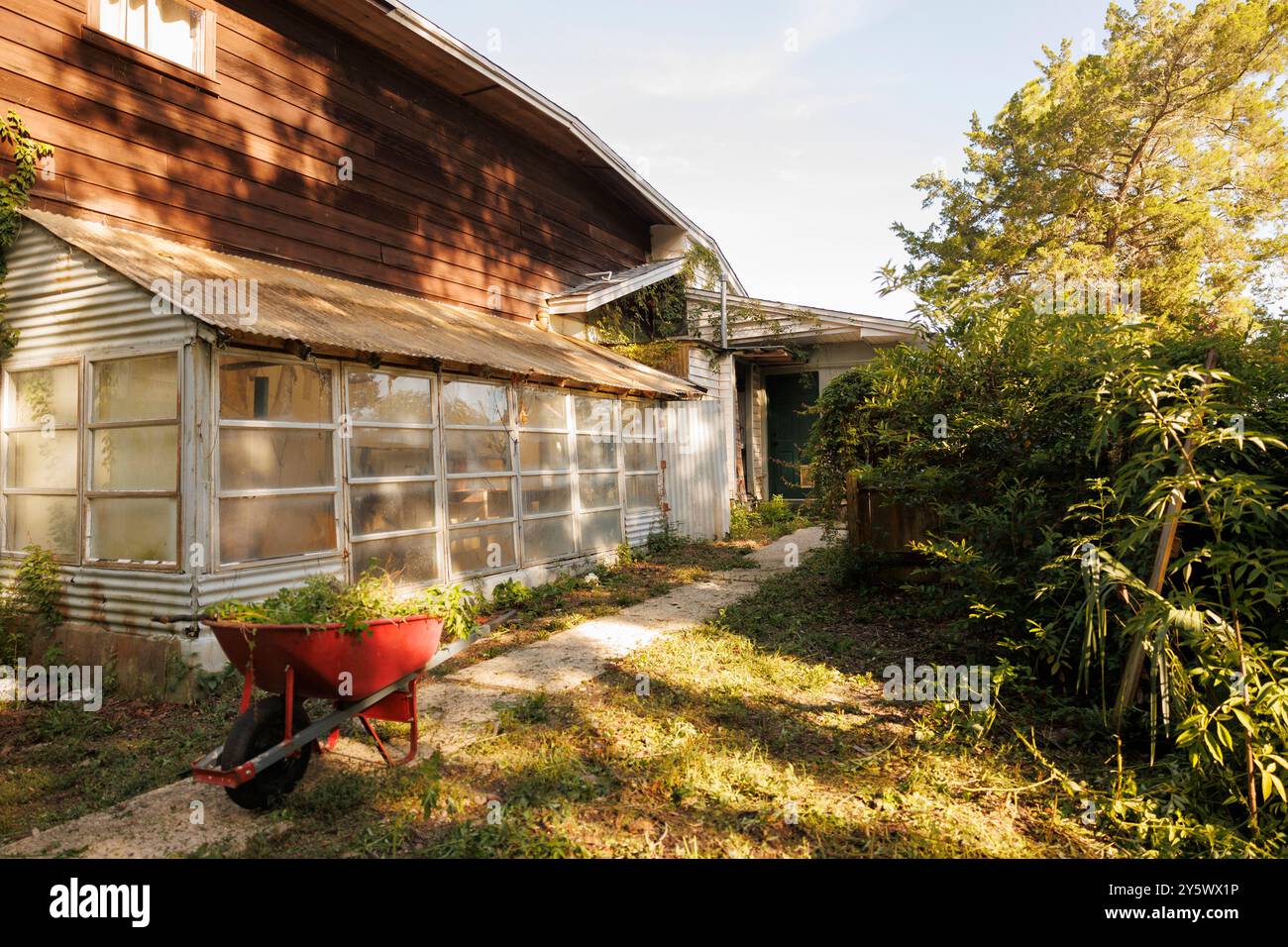 Sonnenlichtfilter auf ein festsitzendes Oberhaus mit bewachsener Vegetation und einer roten Schubkarre im Vordergrund, Florida, USA Stockfoto
