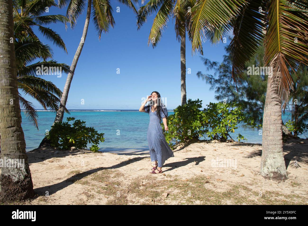 Frau lächelt und geht an einem tropischen Strand mit Palmen und klarem blauen Himmel, Titikaveka, Rarotonga, Cook Islands Stockfoto