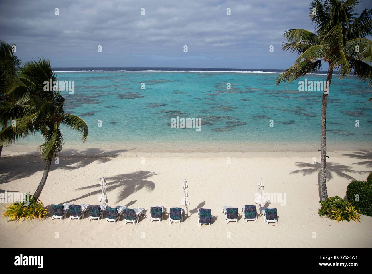 Unberührter Strand mit Liegestühlen unter Palmen mit Blick auf das türkisfarbene Meer, Titikaveka, Rarotonga, Cook Islands Stockfoto