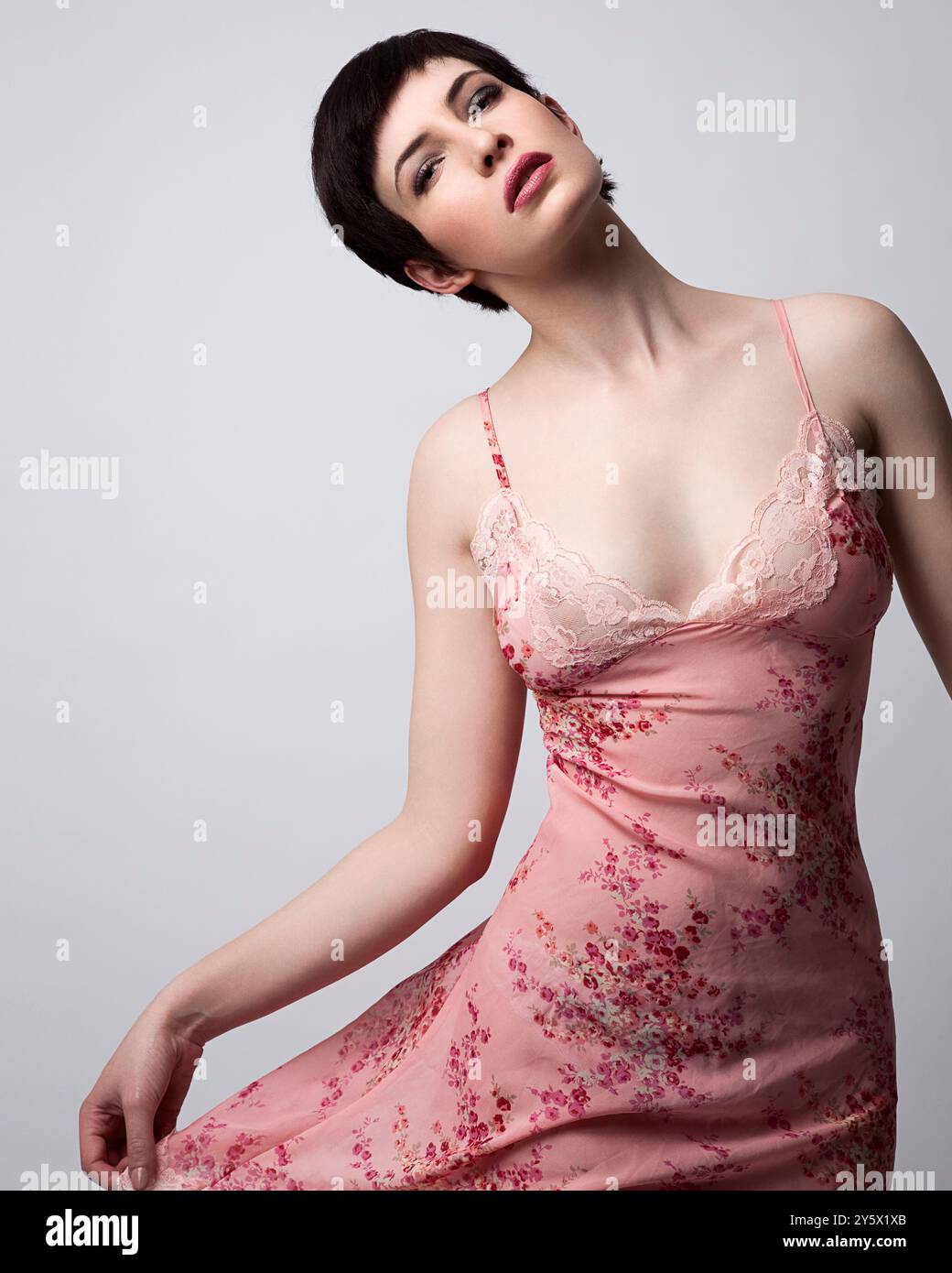 Frau in einem rosa Blumenkleid, das elegant mit einem neutralen Hintergrund posiert. Stockfoto